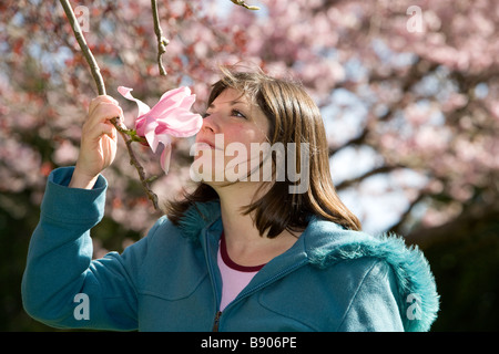 Una bella bruna giovane donna odora un albero di magnolia fiorisce in primavera. Foto Stock