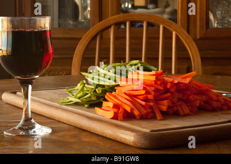 Un tagliere con jullienned le carote e i fagiolini verdi con un coltello e un bicchiere di vino per lo chef Foto Stock