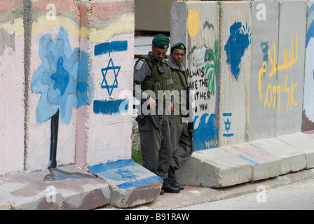 Soldati israeliani guardia lungo le lastre di cemento separando quartiere palestinese di Bab a-Zawiya e H-2 controllo israeliano area in Hebron Cisgiordania Foto Stock