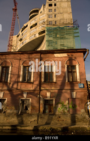 Abbandonata la casa tradizionale nella parte anteriore del grattacielo di costruzione e di gru, a basso angolo di visione, Ekaterinburg, negli Urali, Russia Foto Stock