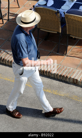 Panoramica di un uomo che indossa cappello di paglia e abbigliamento casual a piedi lungo una strada Foto Stock