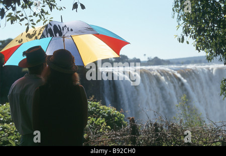 Turisti sotto un ombrello guardando a Victoria Falls sul fiume Zambesi Zimbabwe Foto Stock