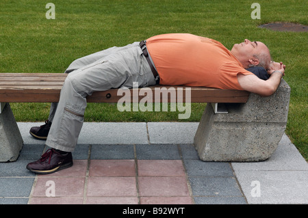 Un uomo addormentato veloce su una sede pubblica Foto Stock