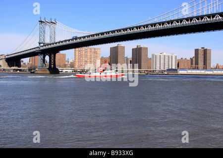 New York City Fire Department imbarcazione di pattuglia sulla East River passa sotto il ponte di Manhattan il collegamento di Brooklyn e Manhattan Foto Stock