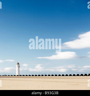 Faro lontano su una spiaggia con l'uomo fatto frangiflutti in primo piano Foto Stock