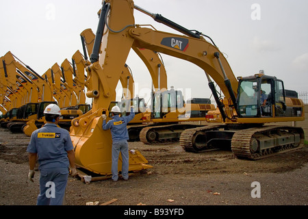 Due ingegneri stanno lavorando su escavatori Caterpillar per installare la benna, parcheggiata nel cantiere aperto per lo storage in pattern ripetitivo Foto Stock