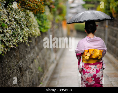 Donna Giapponese in kimono rosa a piedi sotto la pioggia con un ombrellone nero Foto Stock