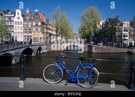 Paesi Bassi, Noord Holland, Amsterdam. Biciclette blu appoggiata contro la ringhiera con Keizergracht e Leidsegracht canali dietro. Foto Stock