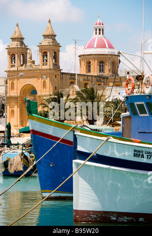 MALTA Marsaxlokk Harbour barche colorate e la chiesa di Nostra Signora del Rosario nella costa sud del villaggio di pesca Foto Stock