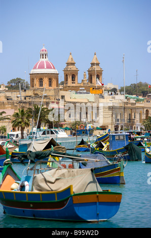 MALTA Marsaxlokk Harbour colorate barche dei pescatori e la chiesa di Nostra Signora del Rosario nella costa sud del villaggio di pesca Foto Stock