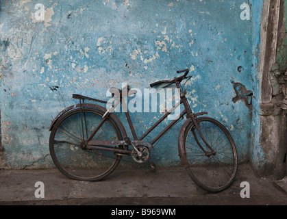 Una vecchia bicicletta arrugginita appoggiata contro una parete blu nella parte antica della città di Ahmedabad, India Foto Stock