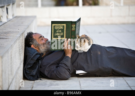 Colpo di un uomo nel centro di Amman in Giordania, disteso sul marciapiede la lettura del Corano. Il suo gatto pazientemente giace sul suo stomaco. Foto Stock