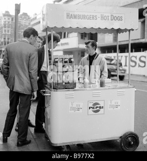 1950s, adatti giovani uomini controllare che cosa cibo e bevande sono disponibili da un piccolo snack o fast food Street vendor a Wardour Street, Londra, Inghilterra, Regno Unito. Foto Stock