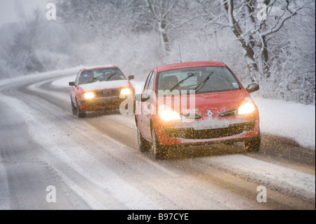 Due auto rosse la guida verso il basso una coperta di neve di strada nella campagna in un giorno di inverni in Inghilterra Foto Stock