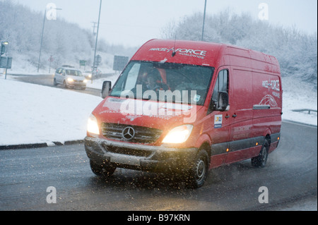 Red royal mail parcelforce van guidando lungo una coperta di neve sulla strada un giorno inverni in Inghilterra Foto Stock