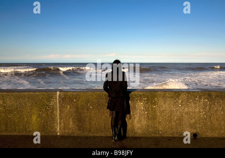 Una giovane donna vestita di nero che guarda al mare nella famosa località costiera di Sandsend, Whitby, North Yorkshire, Inghilterra Foto Stock