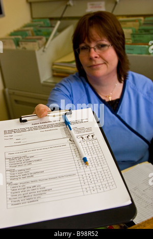 Donna, receptionist dell'ufficio del medico consegna modulo paziente negli appunti Foto Stock
