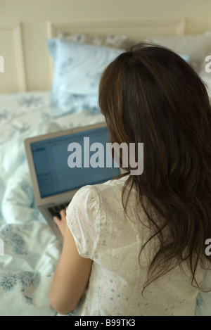 Donna che utilizza sul computer portatile sul letto, vista posteriore Foto Stock