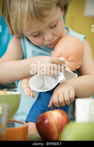 Bambina tergi baby doll's face con un tovagliolo di carta Foto Stock