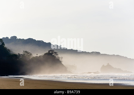 La luce del sole brilla attraverso la nebbia di mattina sulla spiaggia in Dominical, Costa Rica. Foto Stock