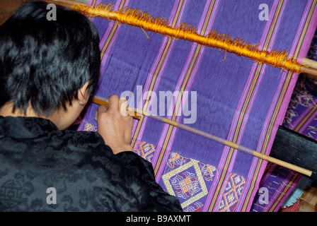 Una giovane donna tesse una lunghezza di splendidamente intricato tessuto di seta utilizzando un dorsalino telaio Foto Stock