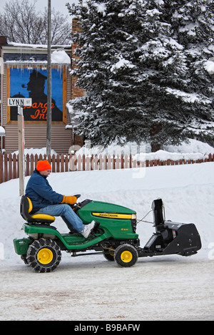 Un uomo con un aratro verde John Deere che rimuove la neve sulla strada invernale della città di Munising Upper Peninsula Michigan USA alta risoluzione verticale degli Stati Uniti Foto Stock
