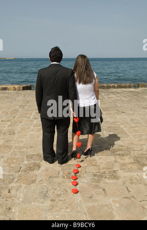 L uomo e la donna in piedi sul mare e il trascinamento di una catena di cuori rossi Foto Stock