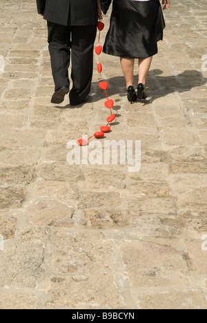 Uomo e donna che cammina verso il mare e il trascinamento di una catena di cuori rossi Foto Stock