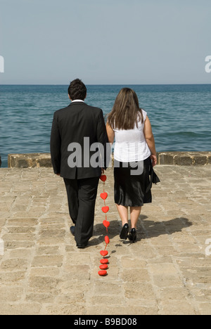 Uomo e donna che cammina verso il mare e il trascinamento di una catena di cuori rossi Foto Stock