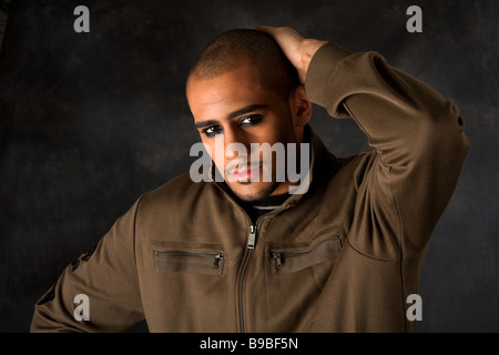 Bello ispanica africana guy accigliata con forte espressione macho e occhi scuri nel giubbotto verde e la mano sulla testa Foto Stock