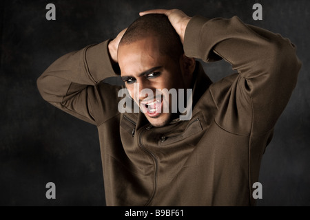 Bello ispanica africana guy accigliata con forte mad macho espressione e occhi scuri nel giubbotto verde e le mani sulla testa Foto Stock