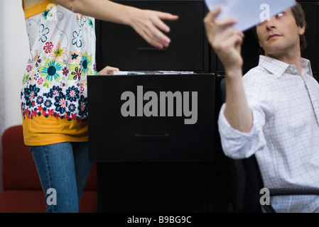 Uomo di consegnare il documento a un collega in piedi da Filing cabinet Foto Stock