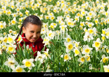 Una giovane e bella gara di misto ragazza a giocare in un campo di narcisi Foto Stock