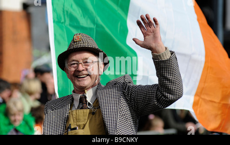 Birmingham San Patrizio Parade, Digbeth, Birmingham, Inghilterra, Regno Unito. Un membro della sfilata onde e sorrisi con bandiera Foto Stock