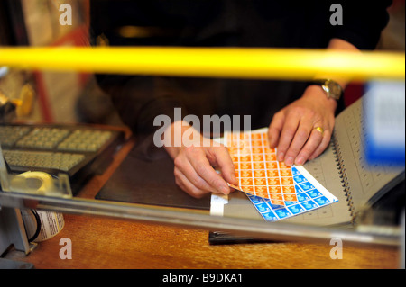 Le mani del post office contatore ordinamento del personale e la vendita di francobolli a in un ufficio postale locale in Bridestowe, Devon, Regno Unito. Foto Stock