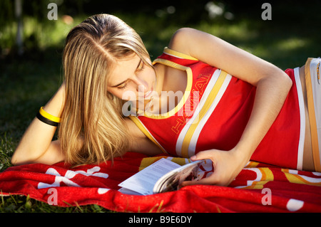Giovane donna in giardino la lettura e il relax sull'asciugamano rosso Foto Stock