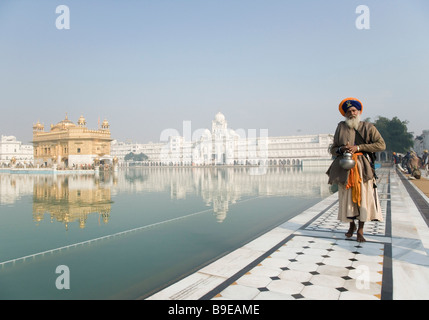 La religione sikh uomo in abbigliamento tradizionale in piedi nei pressi di un laghetto con un tempio in background, Tempio Dorato, Amritsar Punjab, India Foto Stock