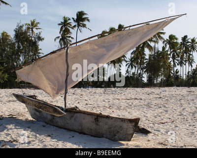 Locale canoa outrigger o ngalawa (spesso erroneamente chiamato dhow) con parti parzialmente arrotolata vela sulla spiaggia sabbiosa tropicale Foto Stock