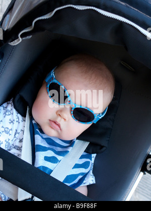 Giovane maschio bambino in una carrozzina buggy indossando occhiali da sole vestita di azzurro angolato Foto Stock