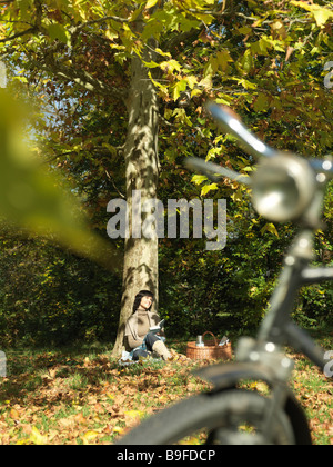 Donna matura appoggiata contro l'albero in posizione di parcheggio Foto Stock