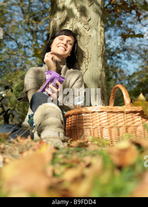 Basso angolo di visione della donna matura in appoggio contro la struttura ad albero e sorridente Foto Stock