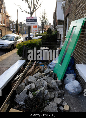 Rifiuti, macerie, rifiuti di cantiere al di fuori di una proprietà di essere rinnovato a Londra. Proprietà confinanti per la vendita in background. Foto Stock