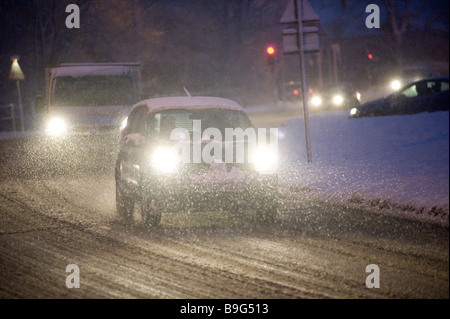 Auto guidando lungo una coperta di neve strada di notte durante il periodo invernale in Inghilterra Foto Stock