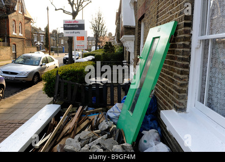 Rifiuti, macerie, rifiuti di cantiere al di fuori di una proprietà di essere rinnovato a Londra. Proprietà confinanti per la vendita in background. Foto Stock