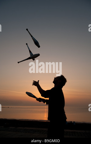 Un uomo in silhouette pratica di giocoleria con 4 club al tramonto su una spiaggia in riva al mare oceano, Aberystwyth Wales UK Foto Stock