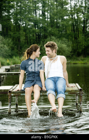 Il lago di coppia seduta ponte piedi acqua splash felice 20-30 anni il raffreddamento al di fuori del bagno-ponte lo sguardo a piedi nudi di rilassamento di contatto Foto Stock