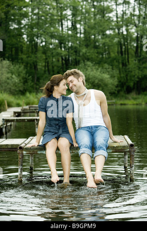 Il lago di coppia seduta ponte piedi acqua splash felice 20-30 anni il raffreddamento al di fuori del bagno-ponte lo sguardo a piedi nudi di rilassamento di contatto Foto Stock