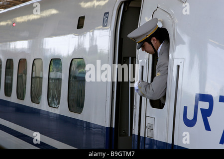 Una guardia controlla il suo orologio mentre la sua serie JR 700 Shinkansen (treno ad alta velocità) si prepara a lasciare la stazione Shin Yokohama in Giappone Foto Stock