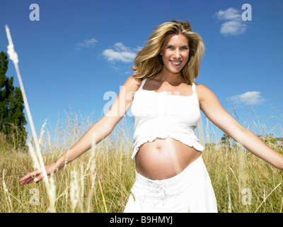 Donna incinta in un campo, sorridente Foto Stock