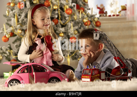 Natale fratelli tappeto sta seduta gioca giocattolo Natale sfondo-tree sfocatura serie persone i bambini 5-7 anni due ragazza Foto Stock